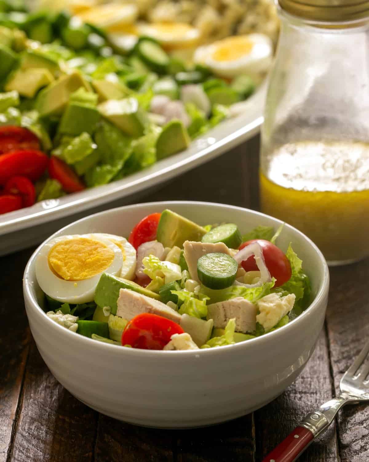 A bowl of Cobb salad wih the serving tray and jar of dressing in the background.