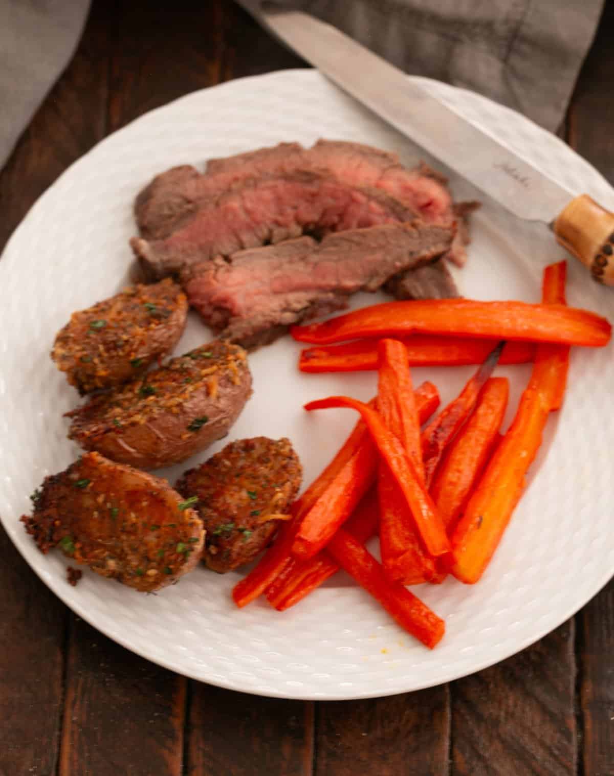Parmesan Roasted Potatoes on a white dinner plate with beef and roasted carrots.