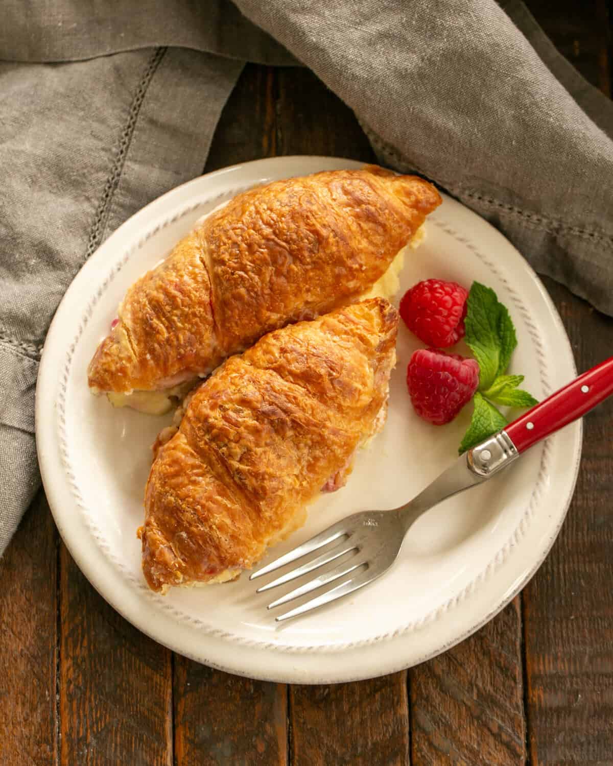 2 berry and cream cheese filled croissants on  a white plate with a raspberry garnish.