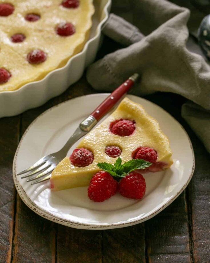 Slice of raspberry clafoutis on a white plate with a red handled fork.