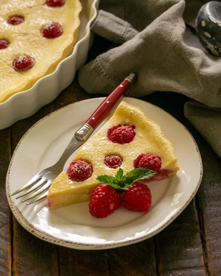 slice of raspberry clafoutis on a white plate with a fork and berries to garnish
