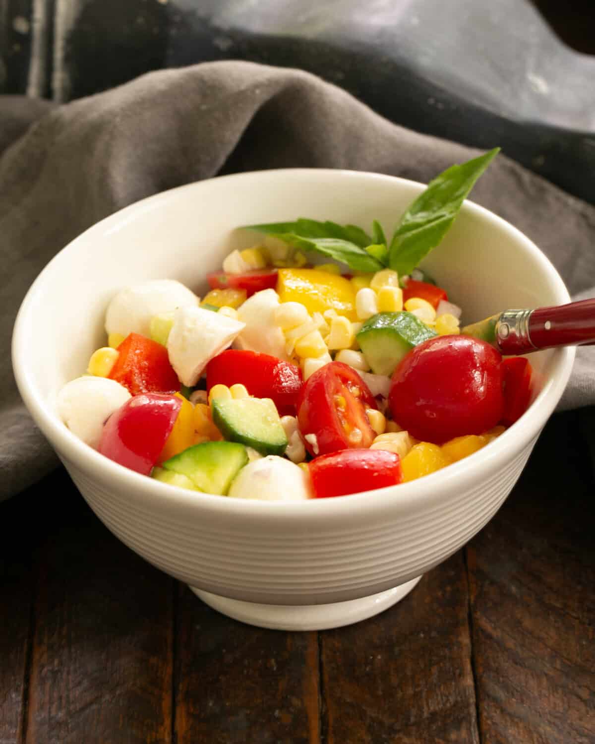 Serving of summer corn salad in a white salad bowl with a red handled fork.